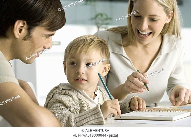 Little boy coloring at table with parents, looking at father