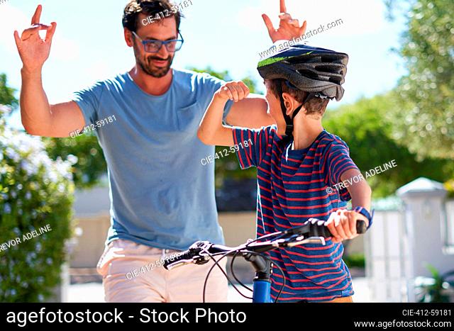 Happy father and son on bike in sunny driveway
