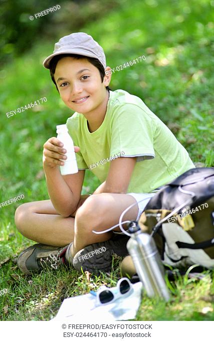 Young boy sitting in the grass and drinking a milk drink