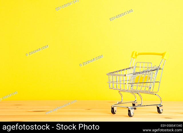 Shopping cart on wooden table with yellow background