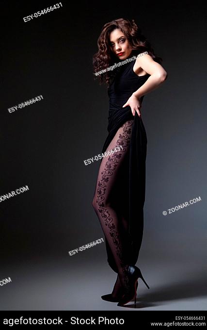 Attractive woman wearing black dress showing the tights. Vertical studio shot