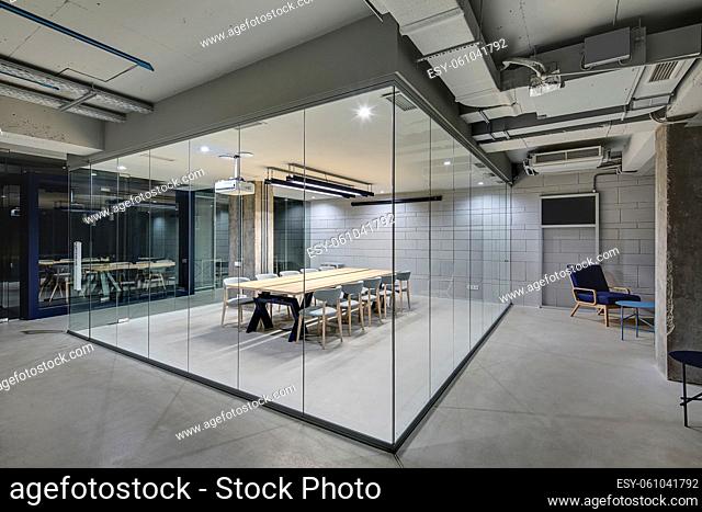 Luminous conference zone in the office in a loft style with brick walls and concrete columns. Zone has a large wooden table with gray chairs and glass walls