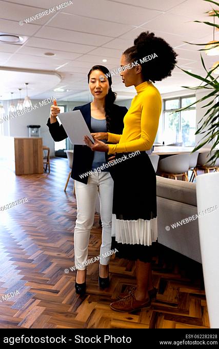 Vertical image of diverse businesswomen with laptop working and talking in office