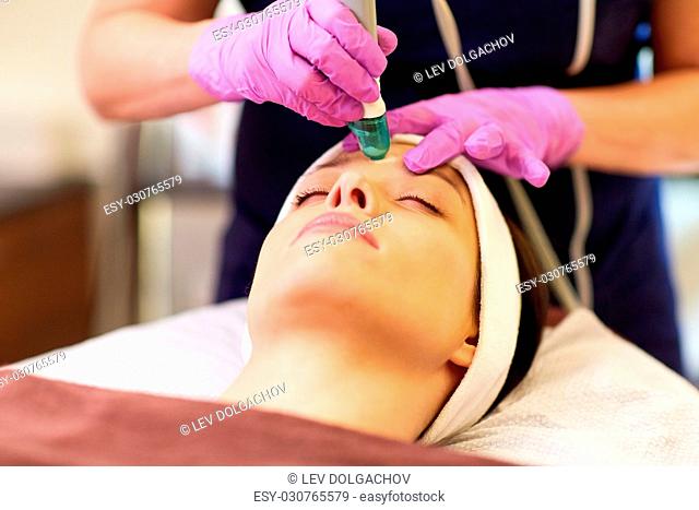 people, beauty, cosmetology, exfoliation and technology concept - beautiful young woman having microdermabrasion facial treatment with crystals in spa