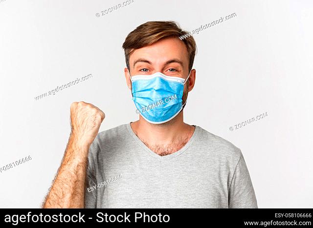 Concept of pandemic, coronavirus and social-distancing. Cheerful caucasian man in gray t-shirt and medical mask, rejoicing from win