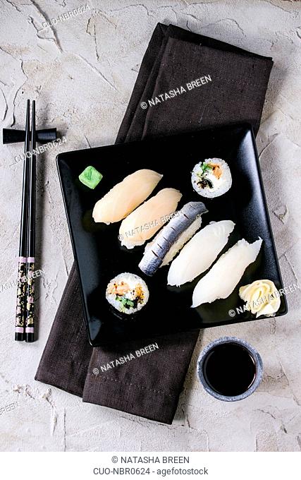 Sushi set nigiri and rolls served on black square plate with chopsticks and soy sauce on gray plastered surface. Flat lay