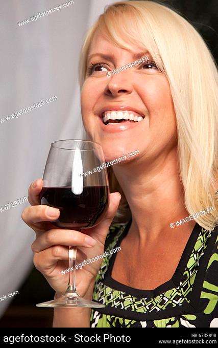 Beautiful blonde smiling woman at an evening social gathering tasting wine