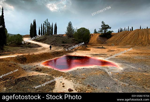 Unrecognized man walking near a Lake with red polluted toxic water of an Abandoned copper mine at Mitsero area in Cyprus