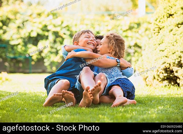 Three little children sitting on a green lawn and talking. Playful siblings at the backyard