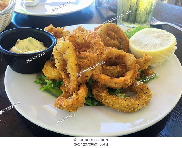 A serving of fried calamari rings on a white plate with a lemon and dipping sauce