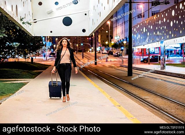 Businesswoman pulling wheeled luggage while walking on platform at night