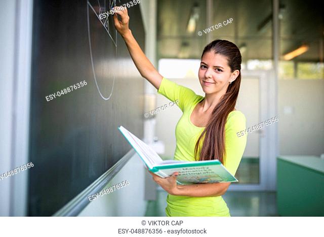 Female university student in front of a blackboard solving a problem - Young teacher in classroom drawing a planimetry problem on the blackboard