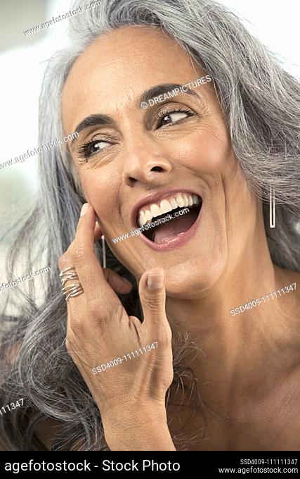 Middle-aged woman with gray hair brushes hair out of her face and looks off camera laughing