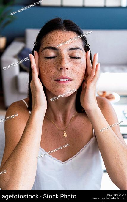 Woman with eyes closed applying moisturizer on face at home