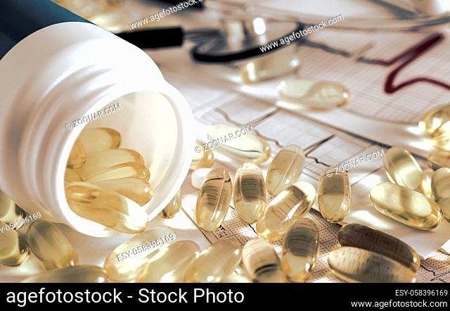 On the table from a white bottle are scattered capsules with yellow medicine. Presented in close-up on the background of an electrocardiogram