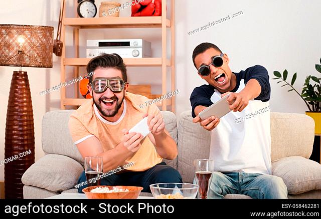 Picture of happy friends playing computer games by using mobile or smart phones. Handsome men sitting on sofa or couch and looking at TV screen