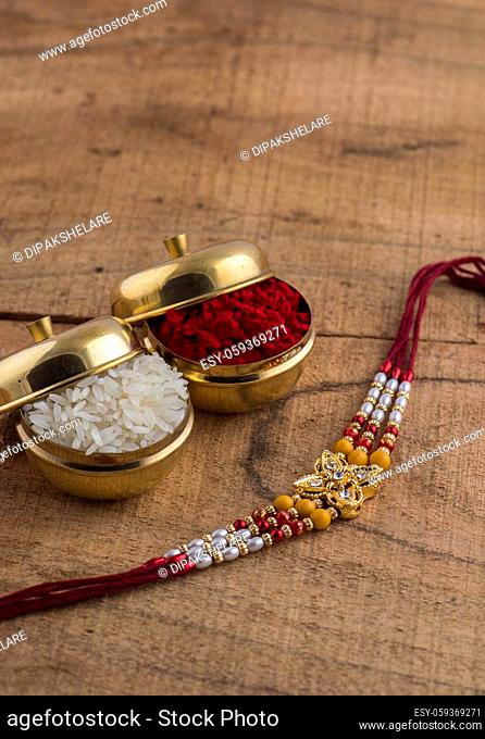 A Rakhi with rice grains and kumkum on wooden background. An Indian festive background