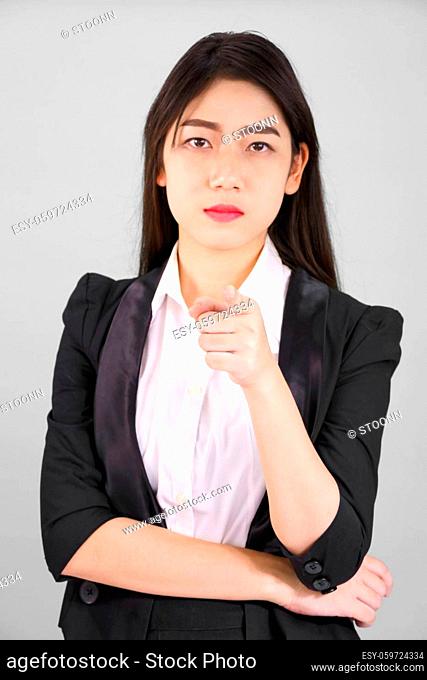 Asian woman in suit looking at camera and pointing finger on gray background