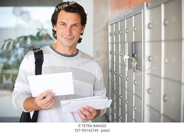 Man standing next to mailboxes and holding letters