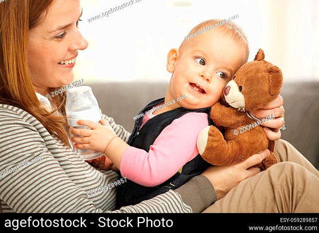 Happy mum and baby girl laughing cuddling holding teddy bear