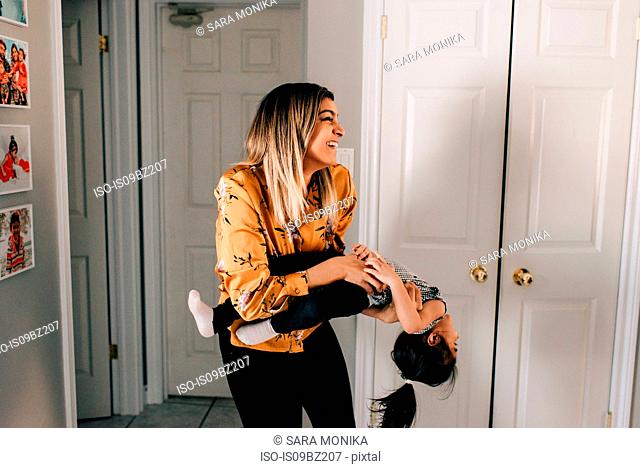 Girl's mother carrying and tickling her in living room