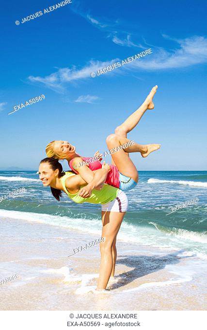 Two women working out on a beach and giving each other a piggyback ride