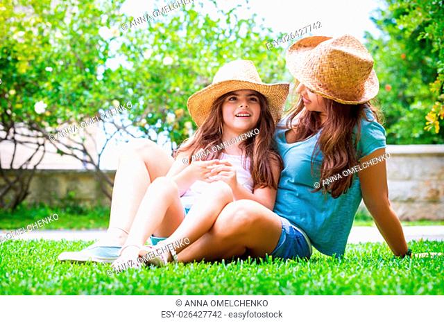 Happy family in the garden, beautiful mother with her little cute daughter sitting on fresh green grass in the backyard, with pleasure spending time together