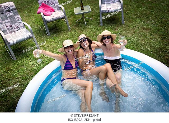 Three mature women sitting in paddling pool, drinking wine, elevated view