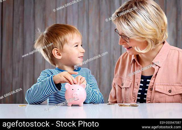 three years old child and young woman sitting at the table with money and piggybank. Happy boy with euro coins. Future childhood and education investment