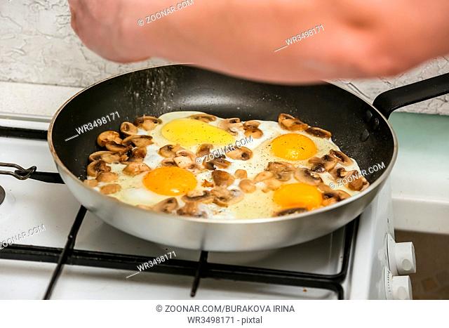 Fried mushrooms champignons and fried eggs in a frying pan on gas stove