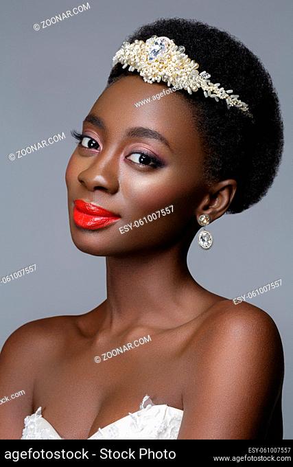Beautiful black skin young woman with red lips in white gown and pearl tiara. Beauty shot on grey background. Copy space