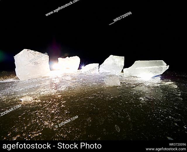 Melting pieces of chopped ice blocks. Strong colorful backlight shine deep cracks, low angle view. Far flat horizon