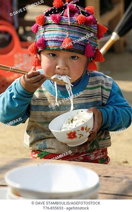 Hmong boy stuffing his face with noodles at market in Tam Duong near Sapa Vietnam