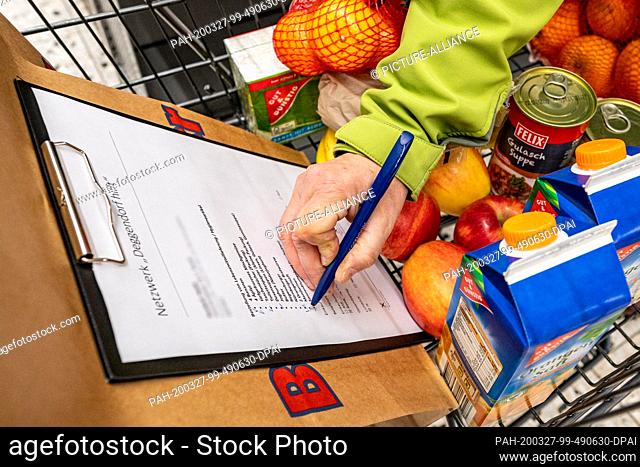26 March 2020, Bavaria, Deggendorf: A helper checks off a shopping list of food. Helpers get food for the elderly and sick