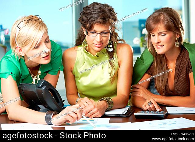 Three attractive businesswomen sitting at meeting room, discussing financial charts on table
