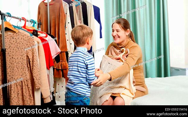 Little toddler boy helping his mother choosing clothes to wear in wardrobe at bedroom