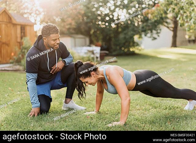 Smiling man looking at woman doing push ups at backyard