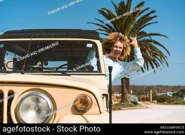 Cheerful blond woman gesturing while sitting in old off-road vehicle on sunny day