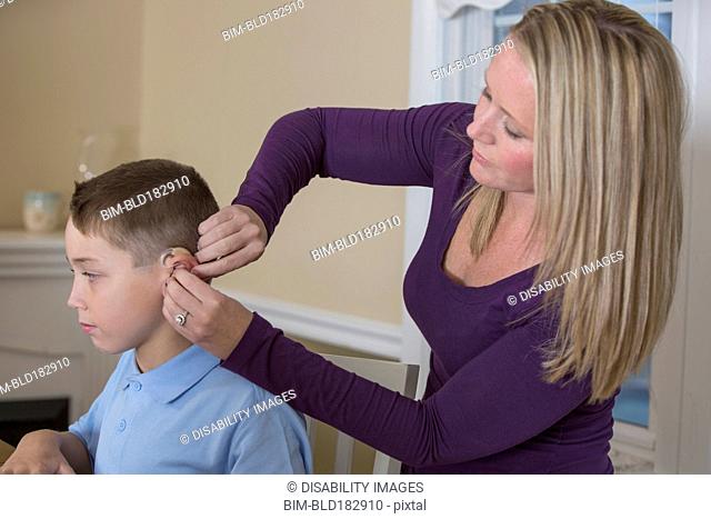 Caucasian mother fitting deaf son with hearing aid
