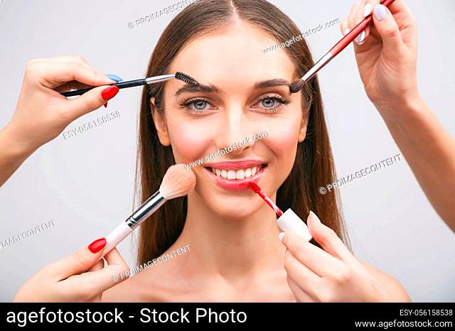 Portrait of a brunette girl getting make-up applied by a makeup with many hands