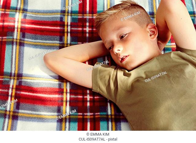 High angle view of boy lying on picnic blanket hands behind head looking away