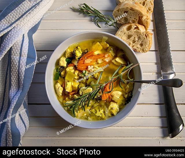 Top View of Chicken Couscous Soup with Fresh Bread on white wood table
