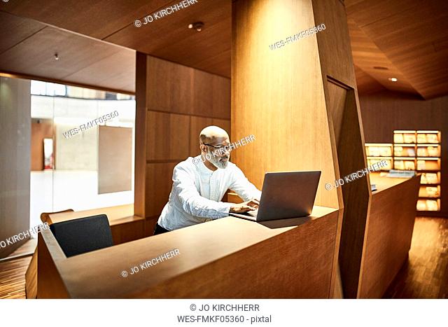 Mature man working on laptop at workspace in library