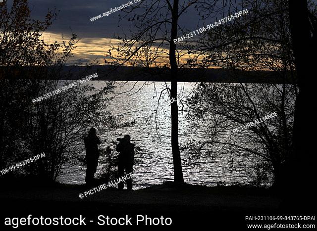 06 November 2023, Bavaria, Inning: Excursionists photograph the Ammersee glistening in the sunshine. Photo: Karl-Josef Hildenbrand/dpa