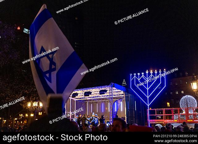 10 December 2023, Hesse, Frankfurt/M.: An Israeli flag is seen in front of a Hanukkah candelabra during the public lighting of the Hanukkah festival in...