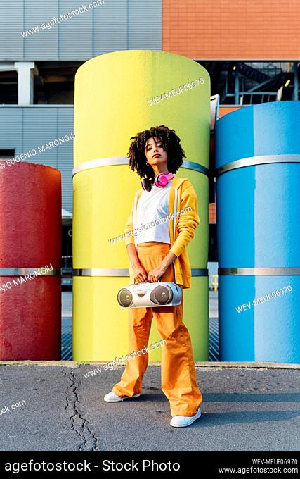 Young woman holding boom box standing in front of colorful pipes