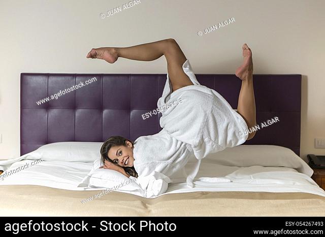 Attractive young female in white bathrobe rolling in bed in hotel room