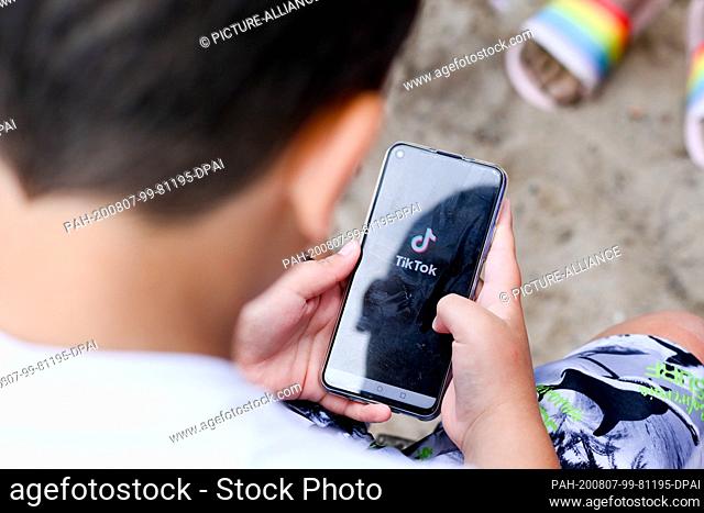 05 August 2020, Berlin: ILLUSTRATION - A boy is holding a smartphone in his hands on a beach, on which the logo of the short video app TikTok can be seen