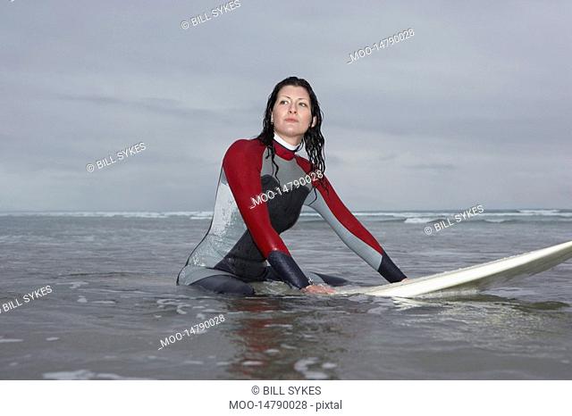 Female surfer sitting on surfboard in water low angle view