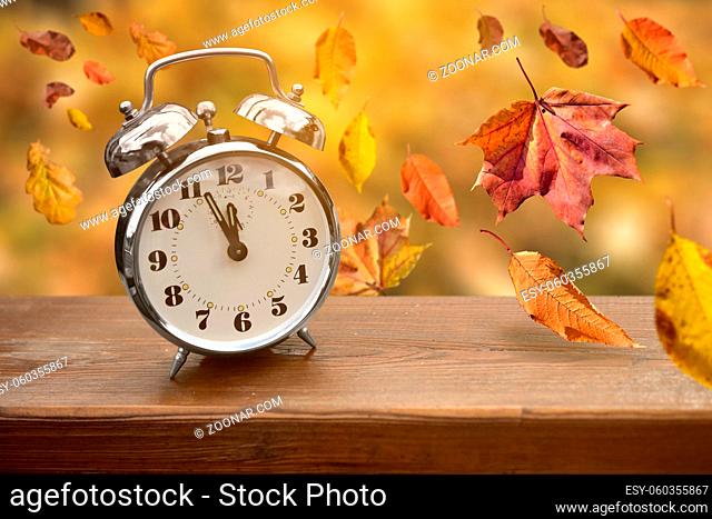 Alarm clock on wooden board just before autumn with leaves